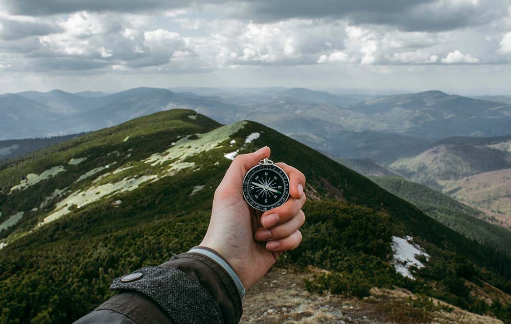 Hand holding a compass with mountain in background