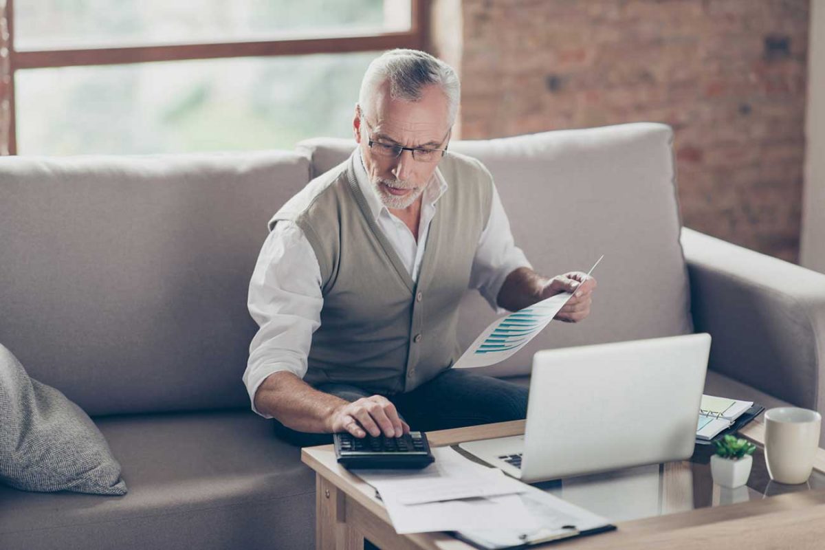 Man sitting on couch with laptop looking at graphs and using calculator