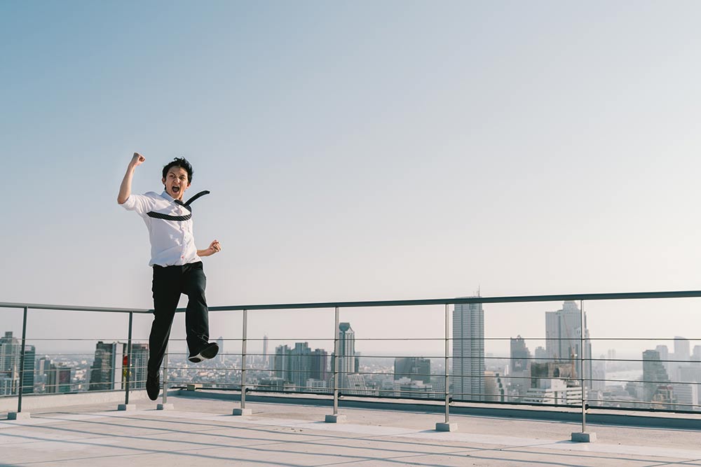 Business man celebrates by jumping in the air on rooftop