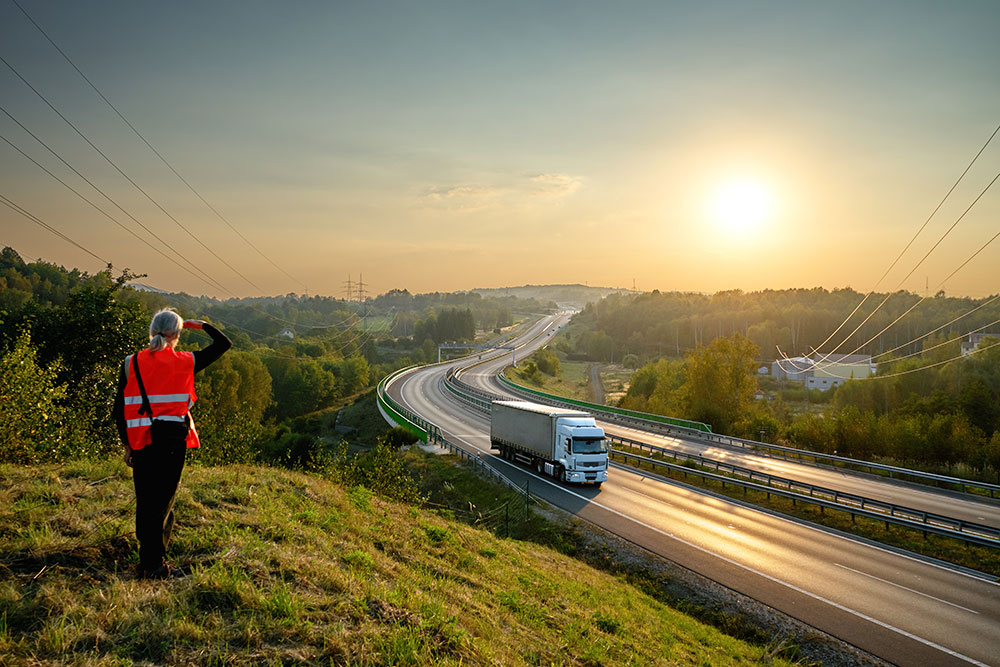 Person in safety vest watching container truck moving down highway